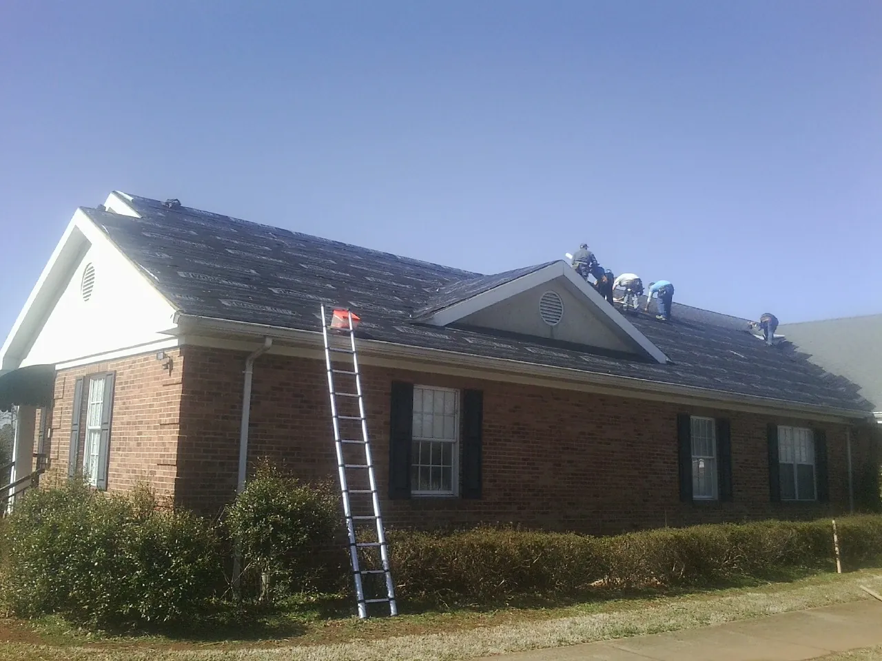 Crew tearing shingles off a brick ranch roof with a ladder set — Metal Roof Repair work by our crew in Auburn
